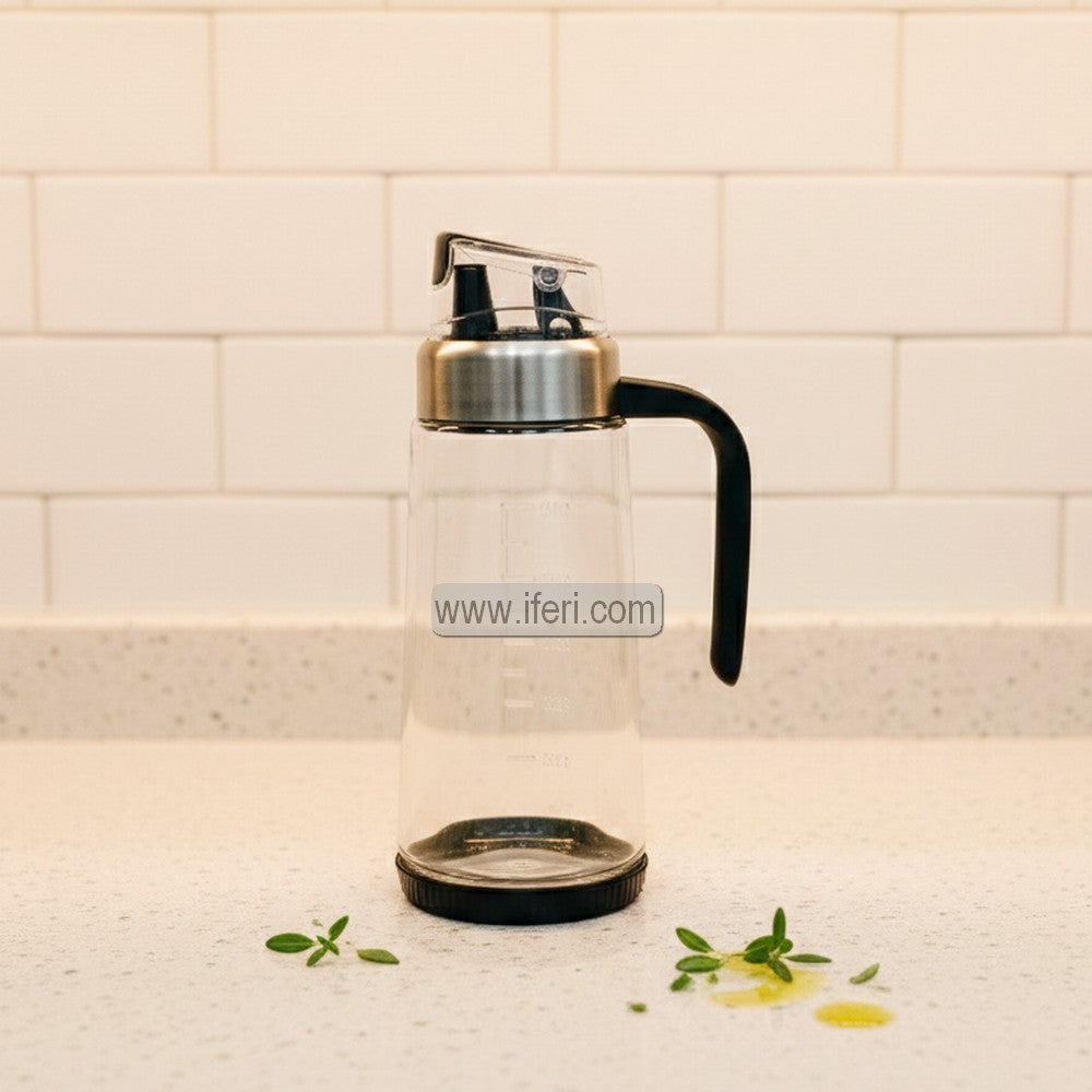 Clear glass oil bottle with black handle and silver cap on a kitchen counter.